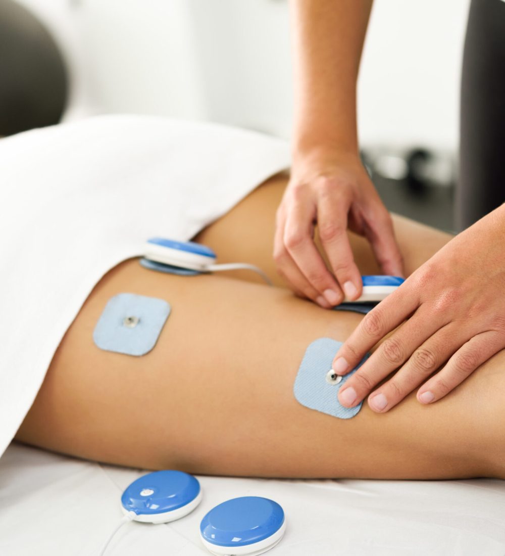 Physiotherapist applying electro stimulation in physical therapy to a young woman. Medical check at the leg in a physiotherapy center.