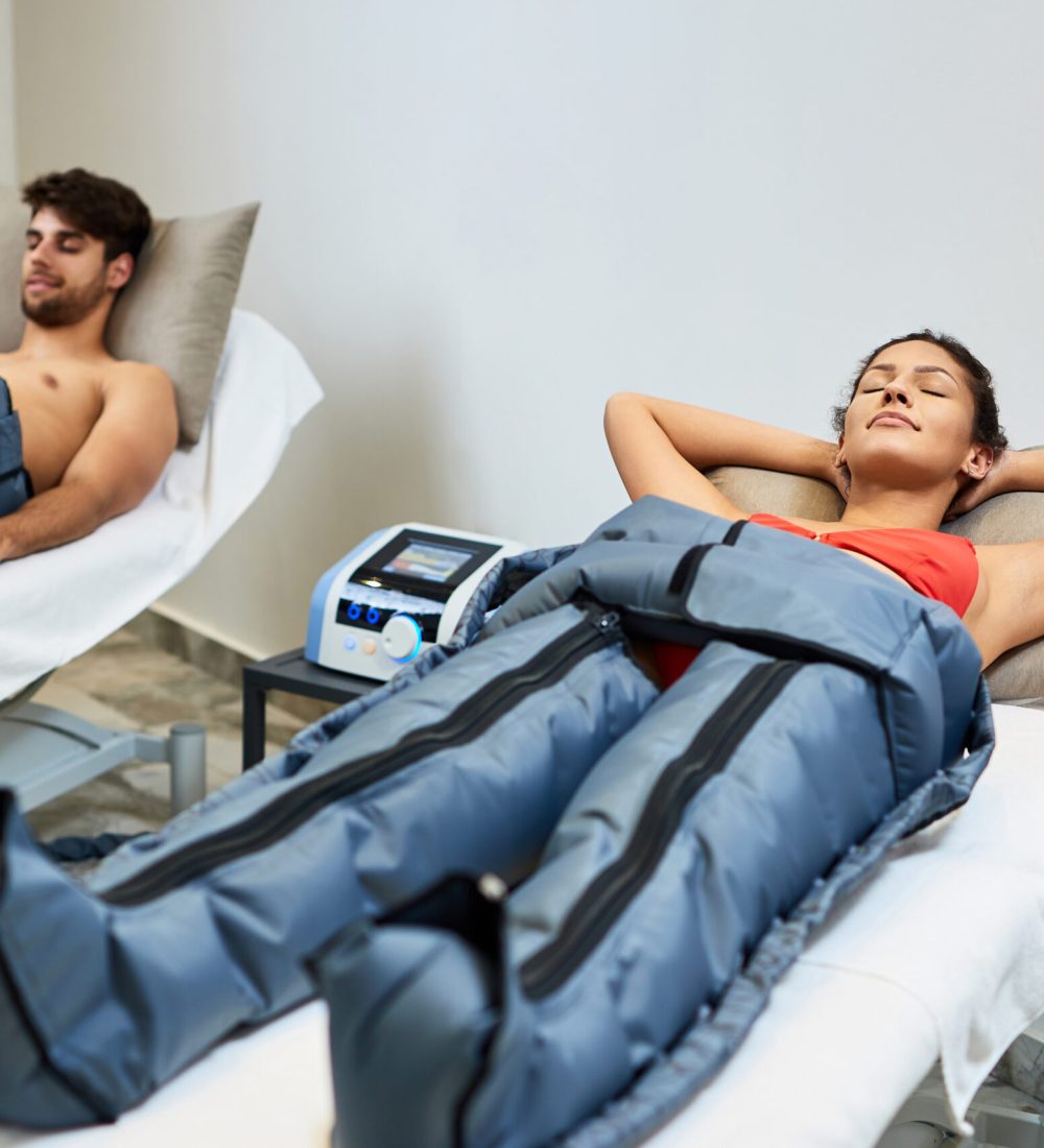 Young couple relaxing during pressotherapy at health spa. Focus is on woman.