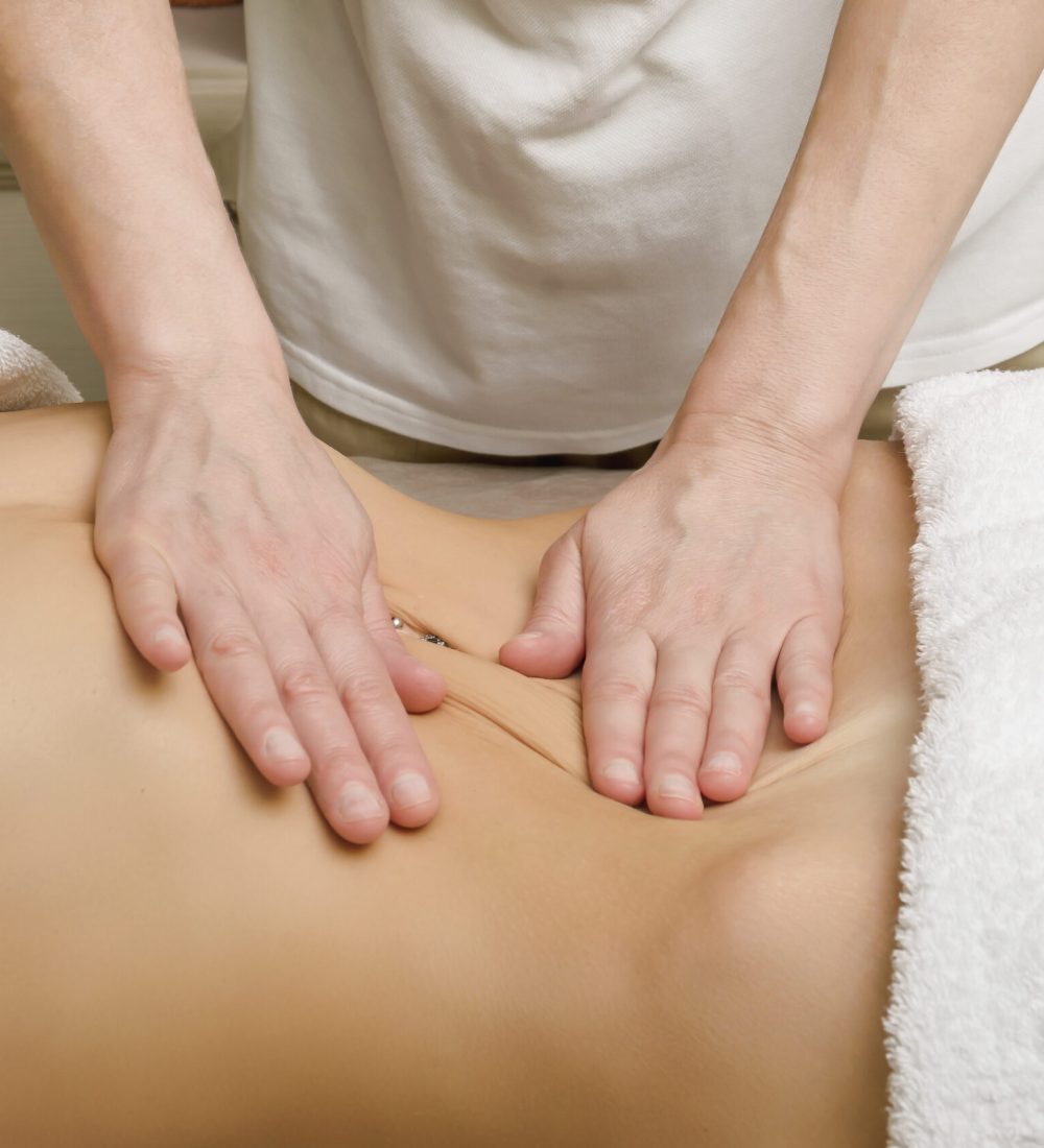 Relaxing professional massage on the female abdomen in the salon. Close-up of female hands of masseur and stomach with piercings